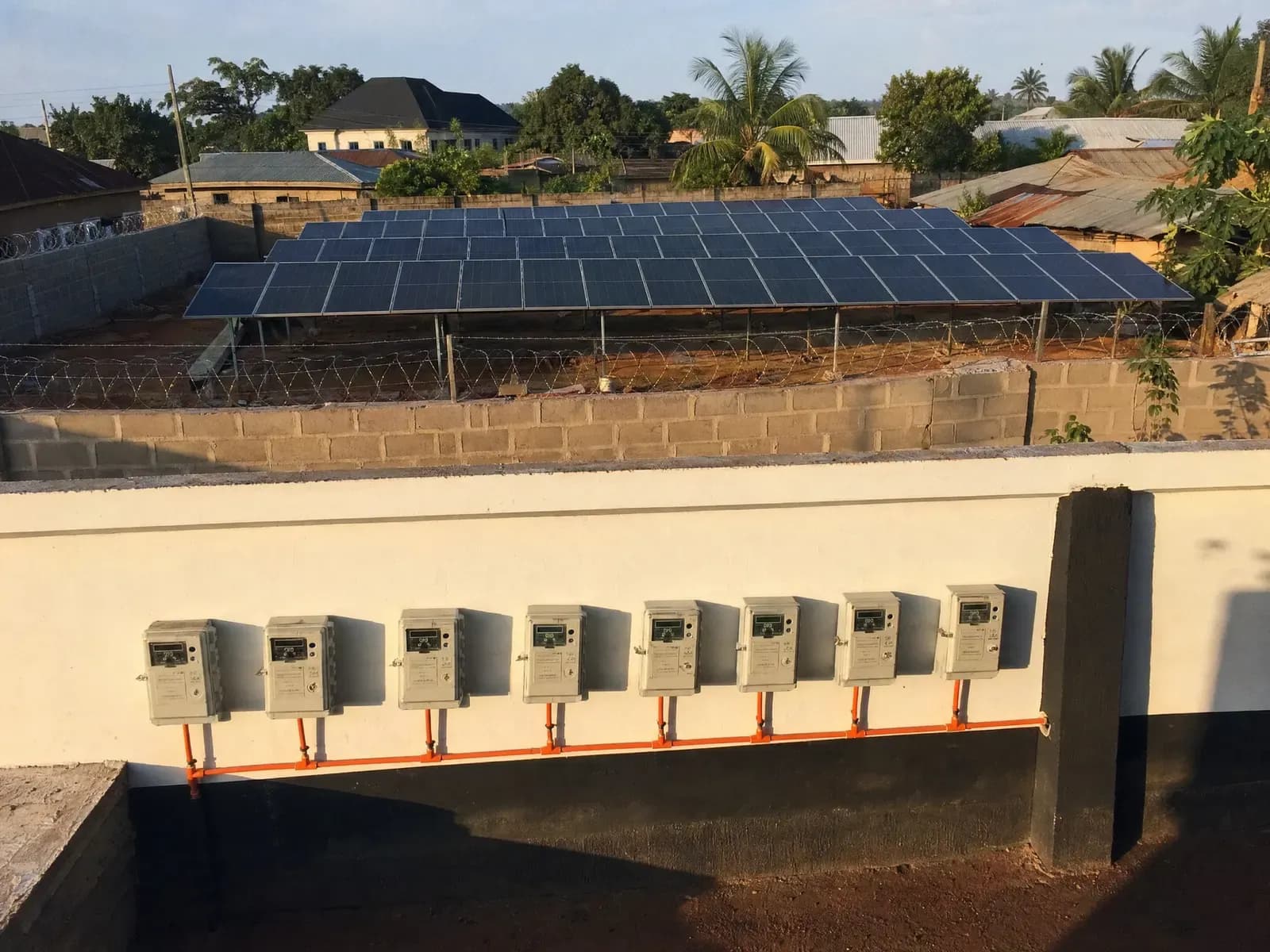 A ground-mounted solar array and a row of prepaid meters in a Nigerian estate compound