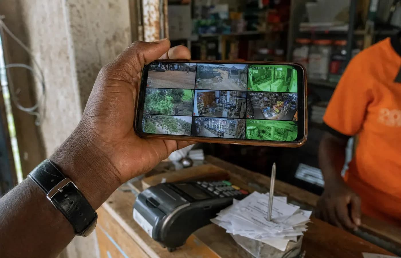 A phone showing nine live camera feeds held over a shop counter